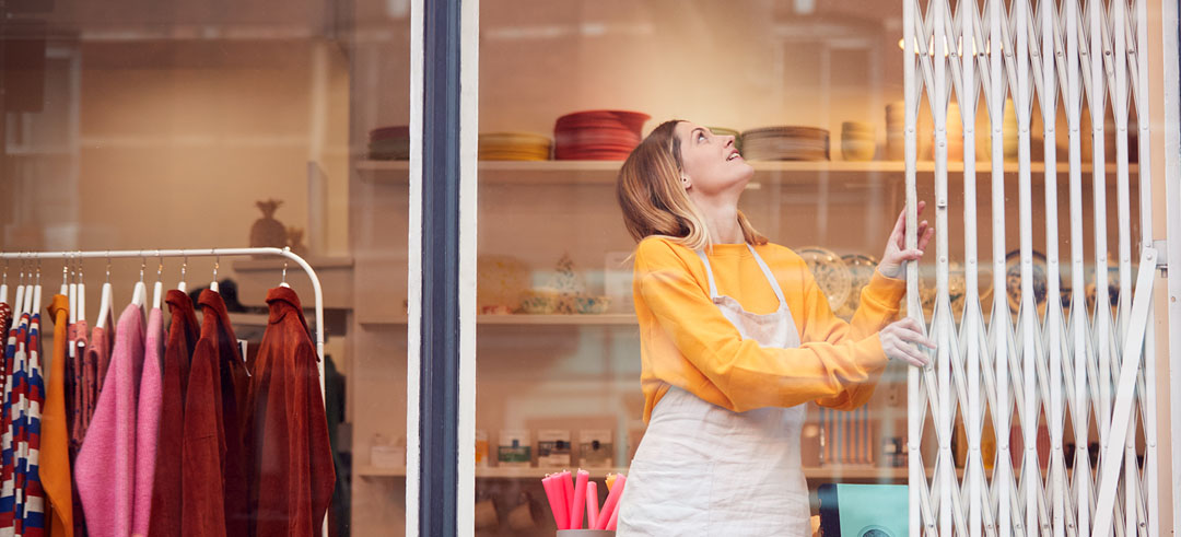 Mujer cerrando con una verja un local comercial