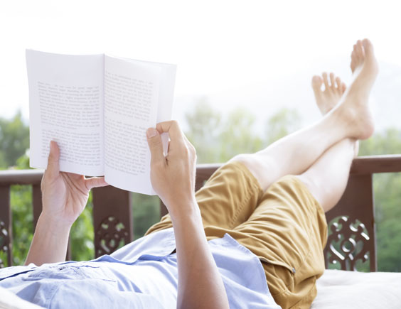 Persona leyendo en una terraza con los pies sobre una barandilla