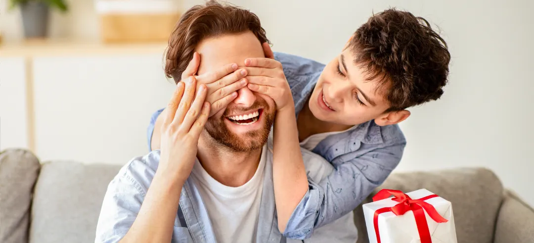 Niño tapando los ojos a su padre mientras sostiene un regalo