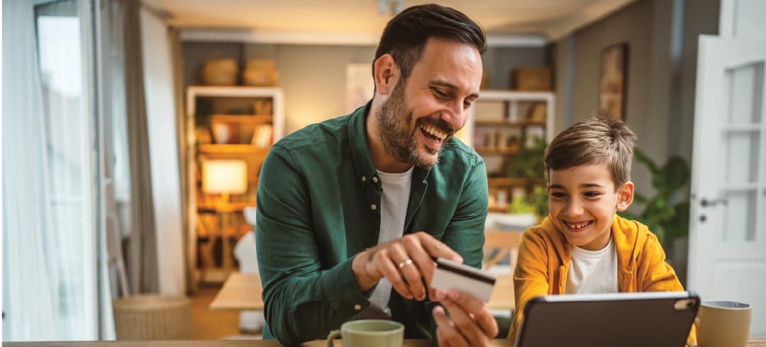 Padre e hijo sonriendo con una tarjeta de crédito y portátil