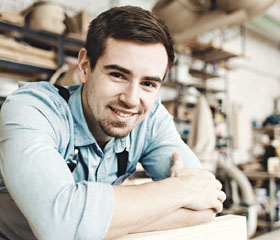 Chico joven sonriendo con los brazos sobre la mesa en su fábrica